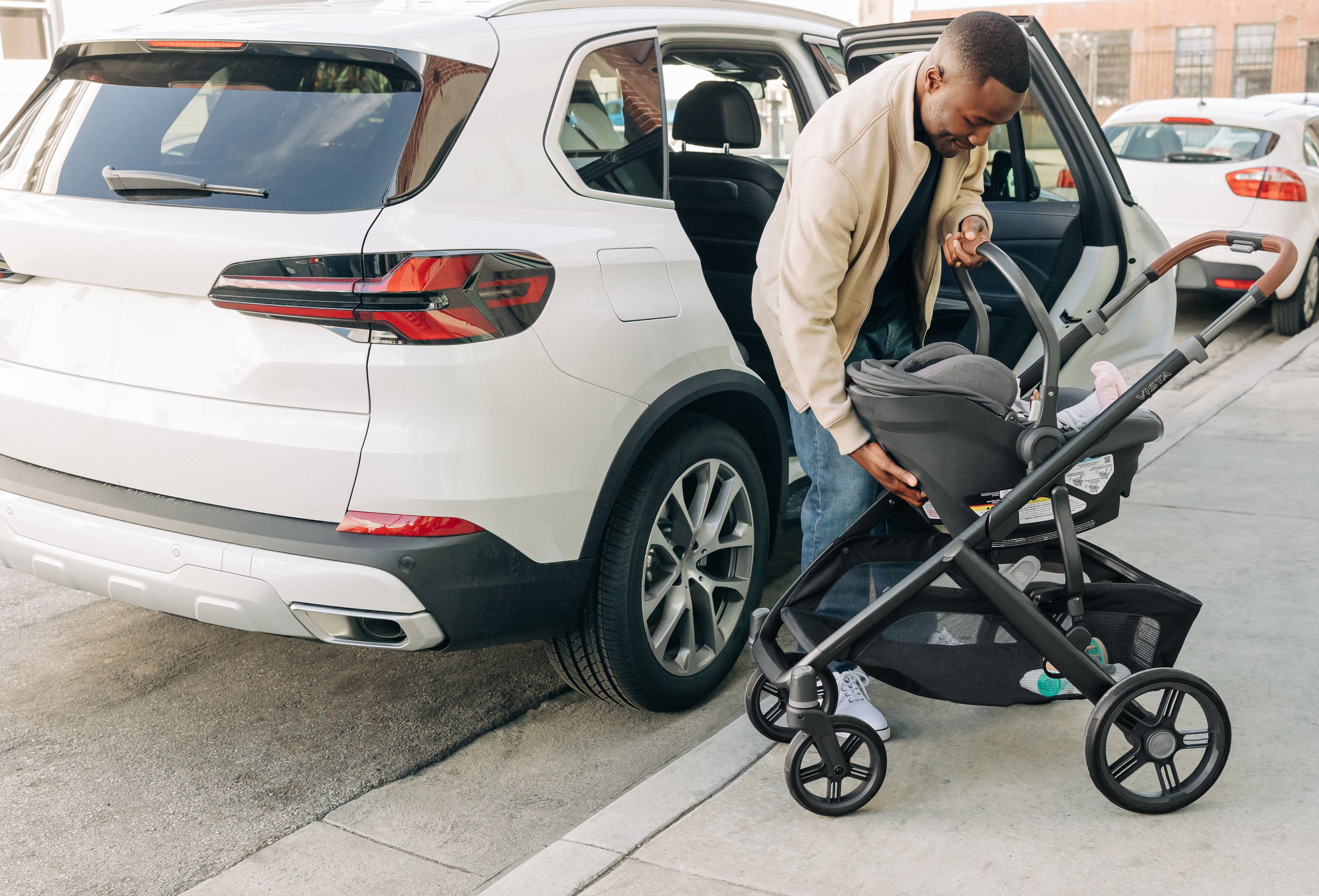 A man sets up the UPPAbaby Vista V3 stroller to accommodate his baby after a car trip, smiling as he prepares for a sunny day outdoors.