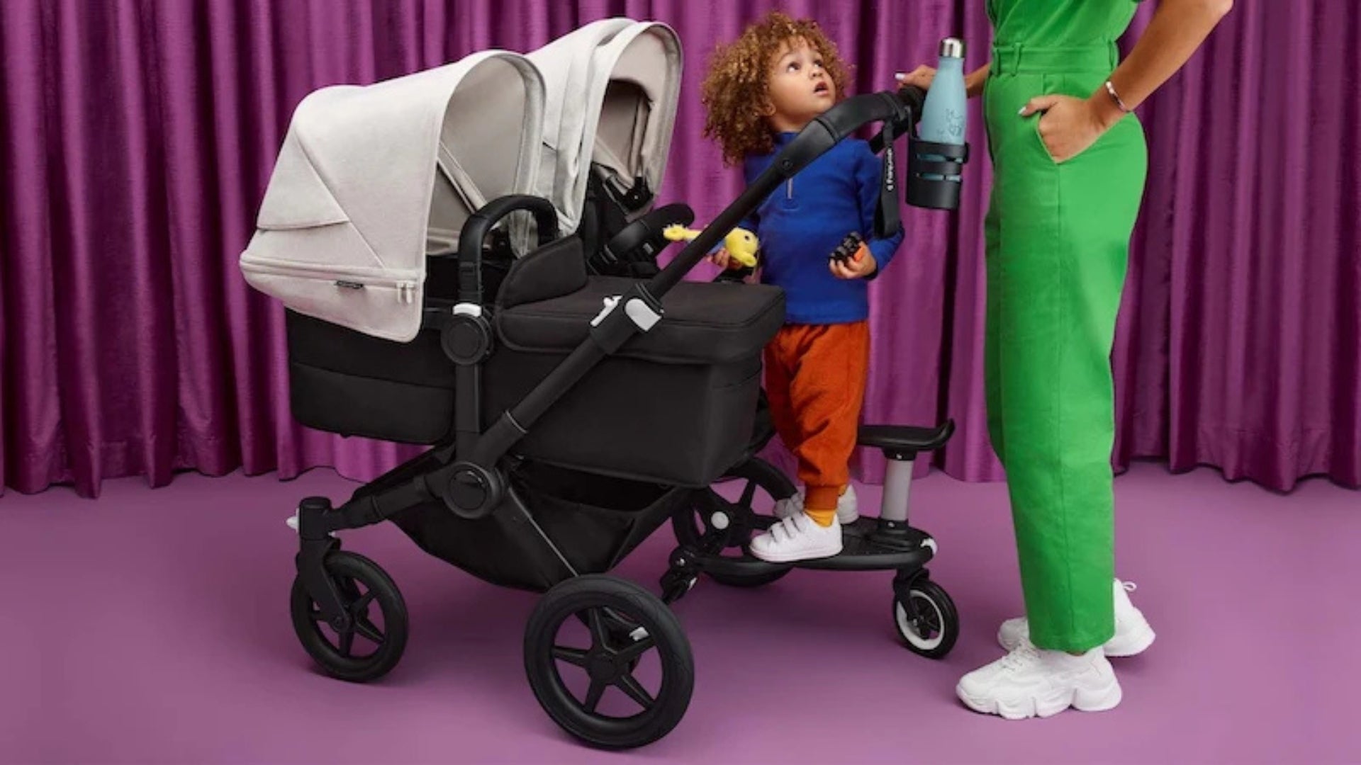 Bugaboo Donkey Twin with two bassinet with newborns and toddler standing on attached ride on board