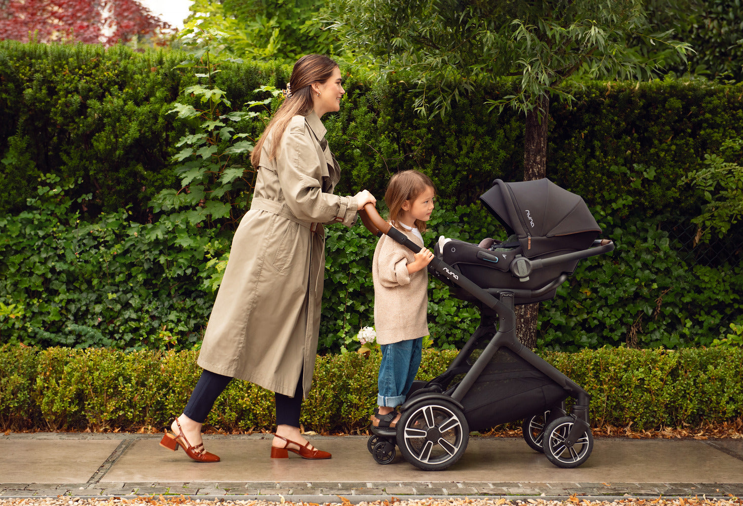 A woman happily pushing the PIPA Urbn Demi Next stroller with a child inside, enjoying a sunny day outdoors.