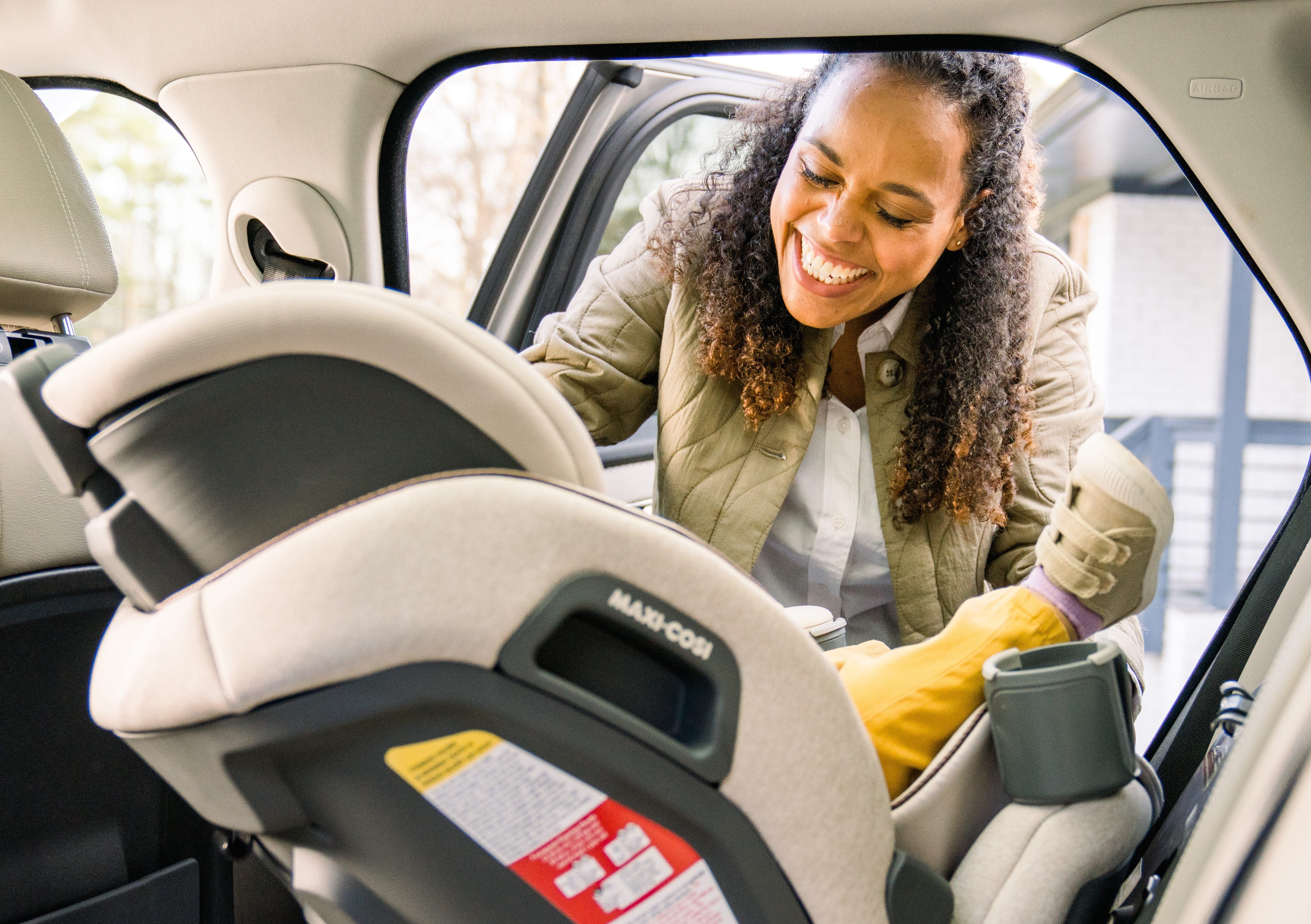 Woman smiling while securing a child in the Maxi-Cosi Emme car seat inside a vehicle.