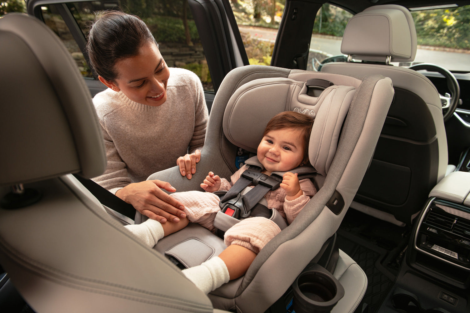 A mother is adjusting her baby in the Nuna Rava car seat inside a vehicle, both of them smiling.
